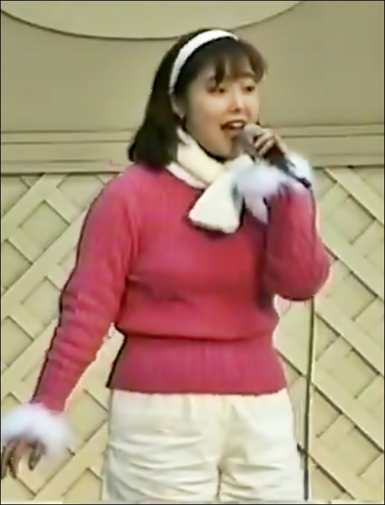 橋本潮、ステージでマイクで歌う、1996年12月28日、ピンクのセーターと白のパンツ